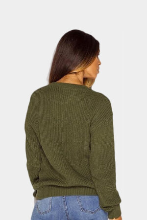 A beautiful woman posing in khaki colored baggy long sleeve knitted plain chunky sweater against solid grey background