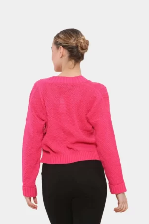Woman wearing punch pink colored chunky aran cable knitted cropped cardigan in grey background